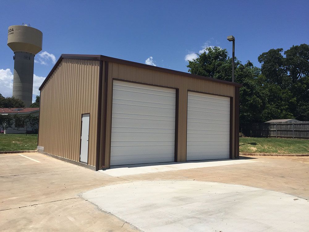 A brown building with two white garage doors and a water tower in the background.