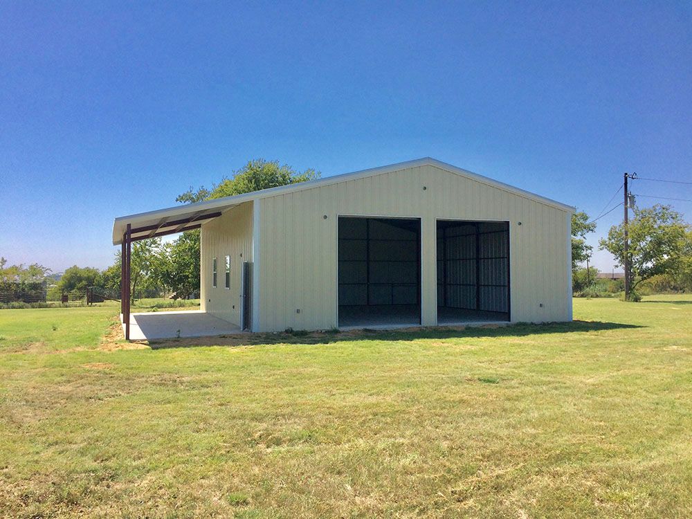 A large white building is sitting in the middle of a grassy field.