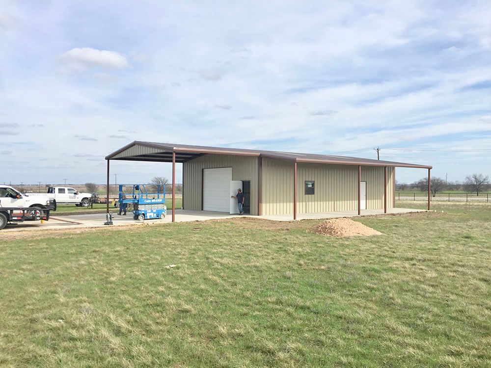 A large metal building is being built in the middle of a grassy field.