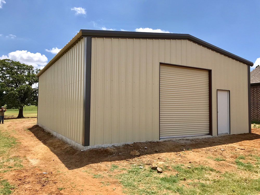 A large metal building with a garage door is sitting in the middle of a dirt field.