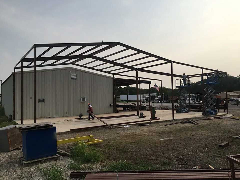 A large metal building is being built in a dirt field.