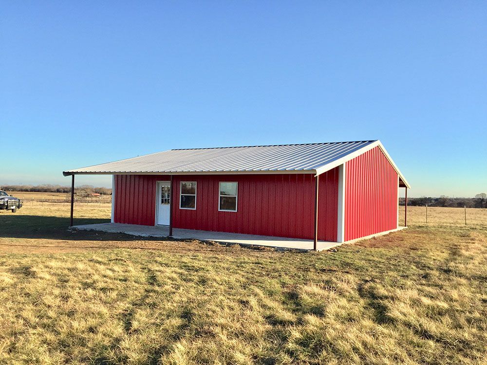 A red barn with a white roof is sitting in the middle of a grassy field.