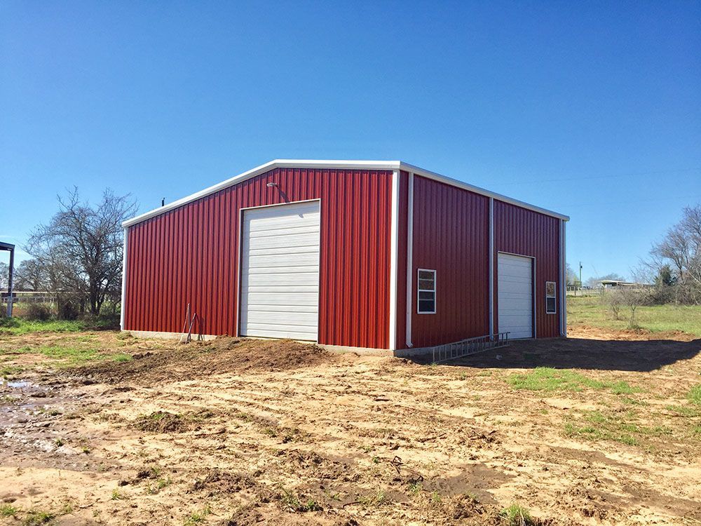 A red metal building with a white door is sitting in the middle of a dirt field.