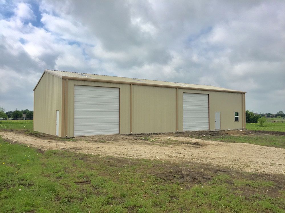 A large building with two garage doors is sitting in the middle of a grassy field.