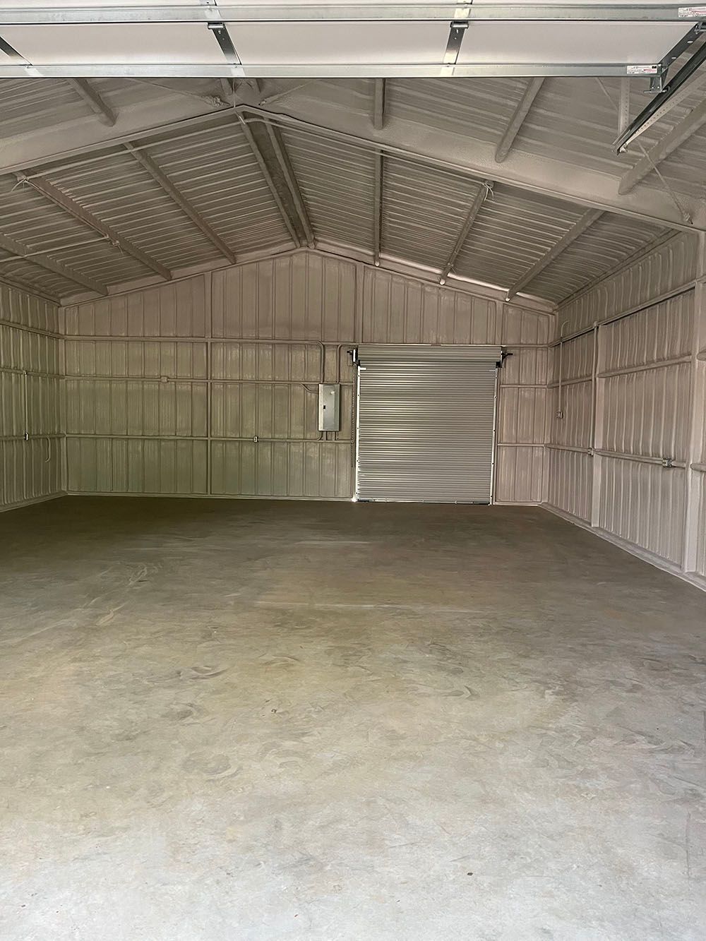 A large empty garage with a concrete floor and a metal door.