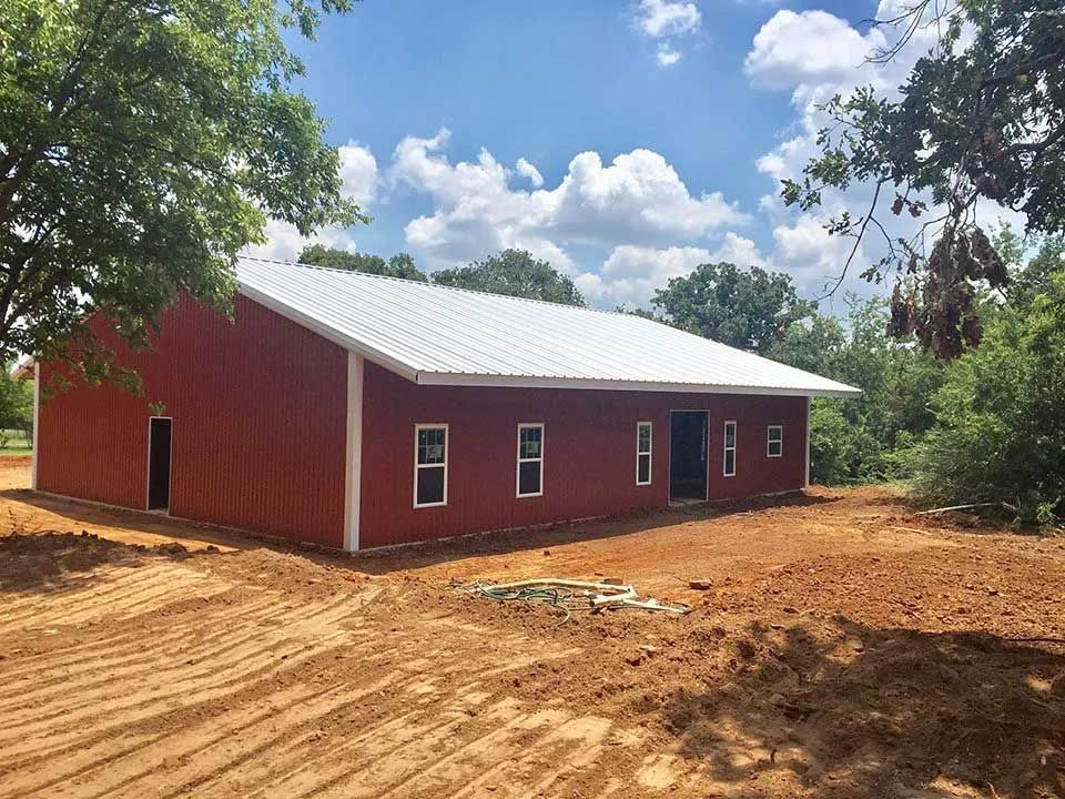 A large red barn with a white roof is sitting in the middle of a dirt field.