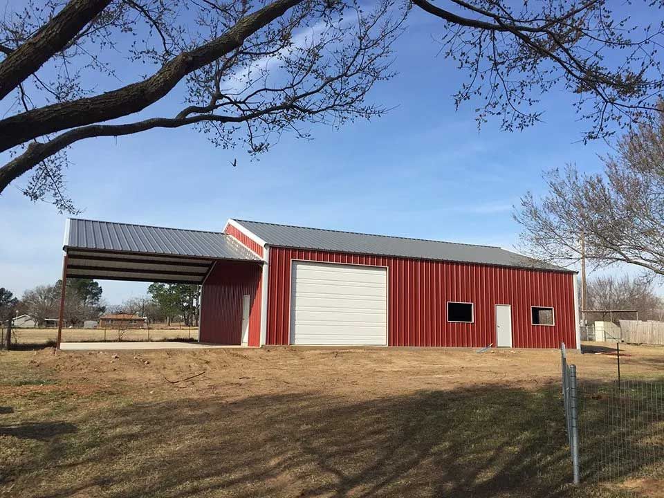 A large red barn with a white door is sitting in the middle of a field.