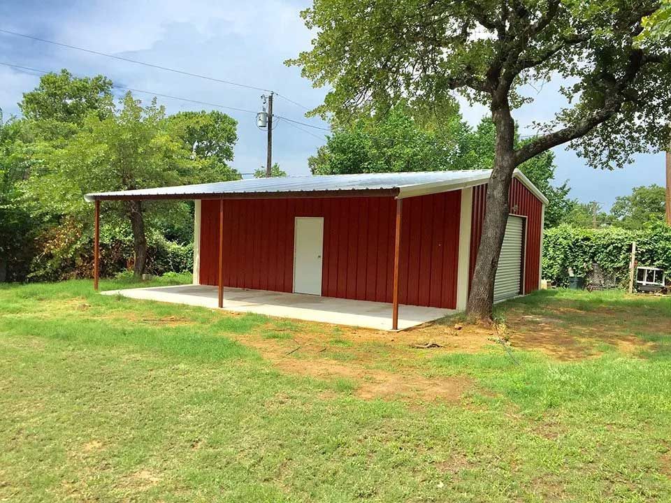 A red barn with a porch is sitting in the middle of a grassy field.