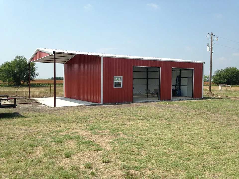 A red barn with a white roof is sitting in the middle of a grassy field.