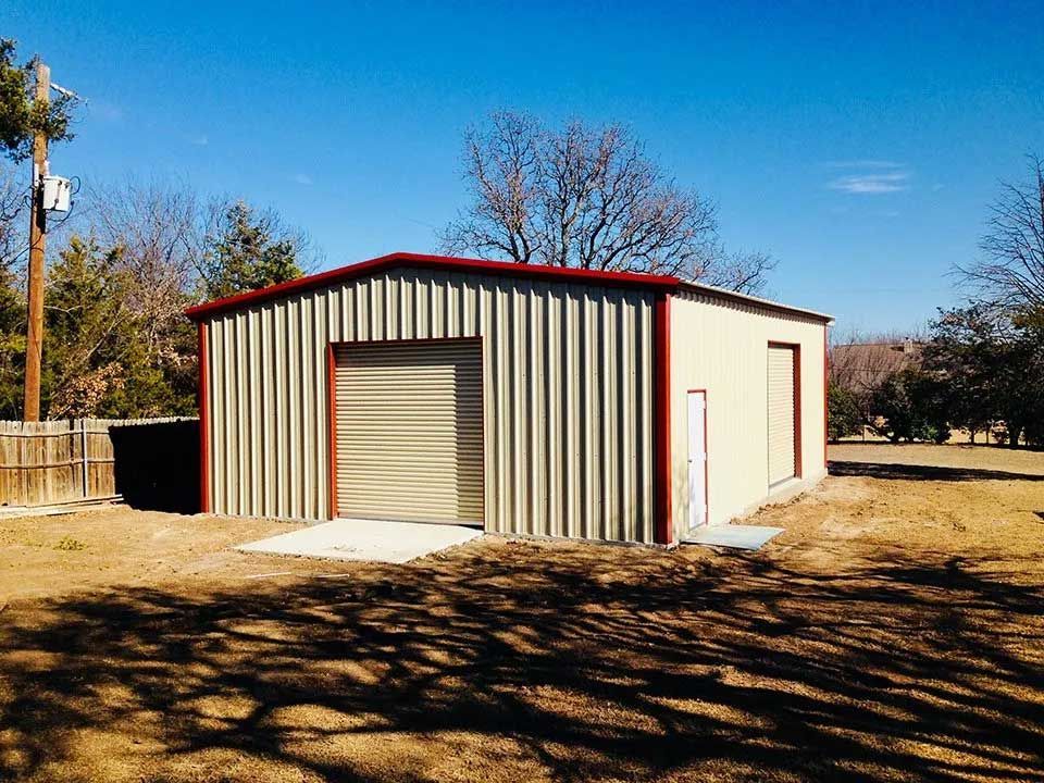 A metal garage with a red trim is sitting in the middle of a dirt field.