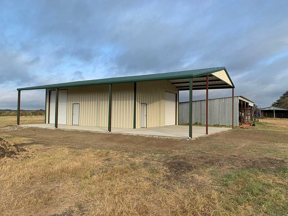 A large metal building with a green roof is sitting in the middle of a field.