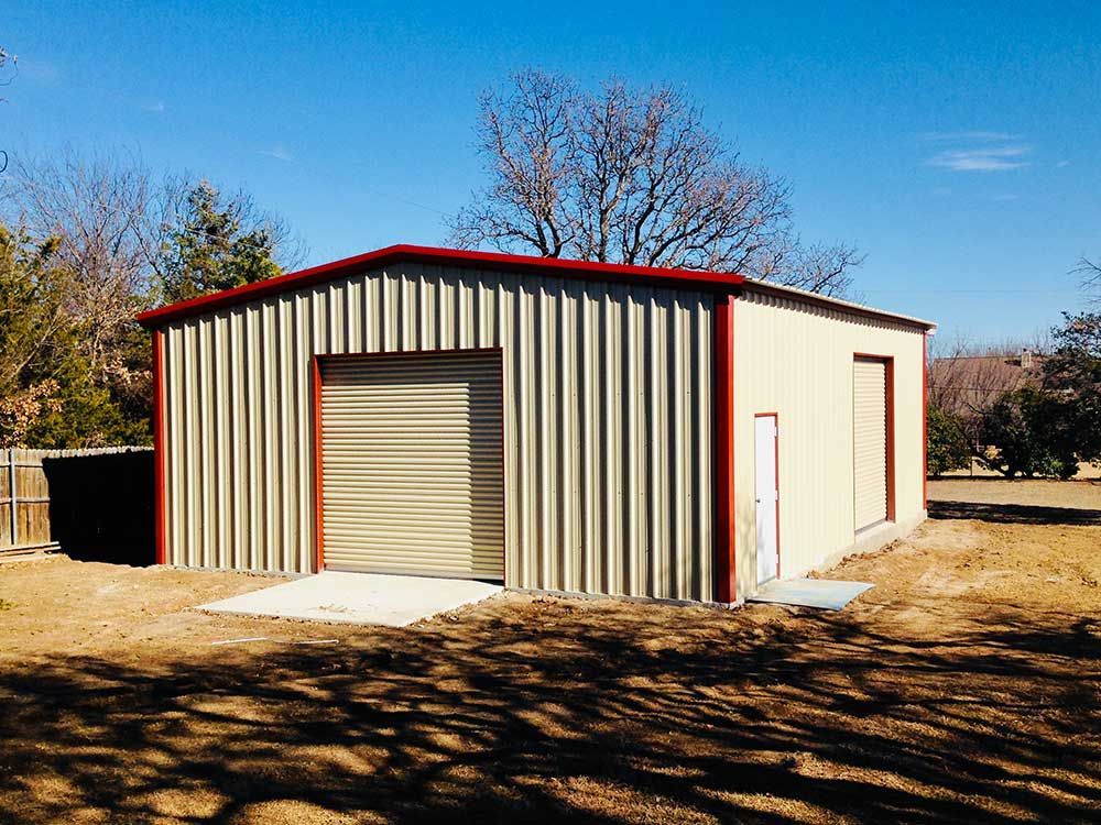 A metal garage with a red roof is sitting in the middle of a dirt field.
