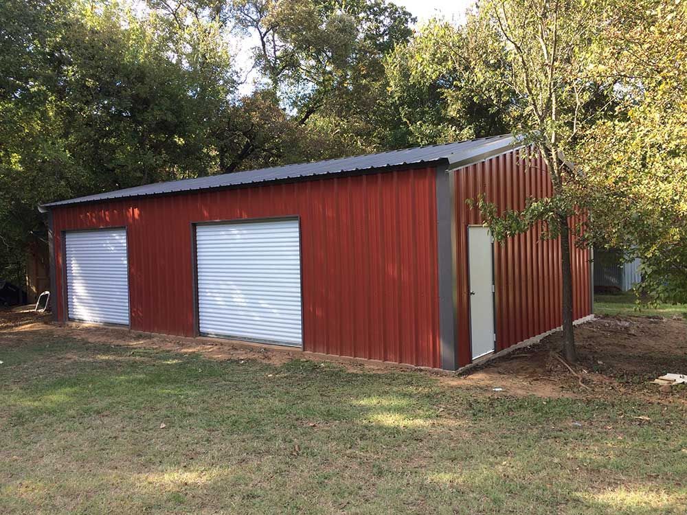 A red metal building with two garage doors is sitting in the middle of a grassy field.
