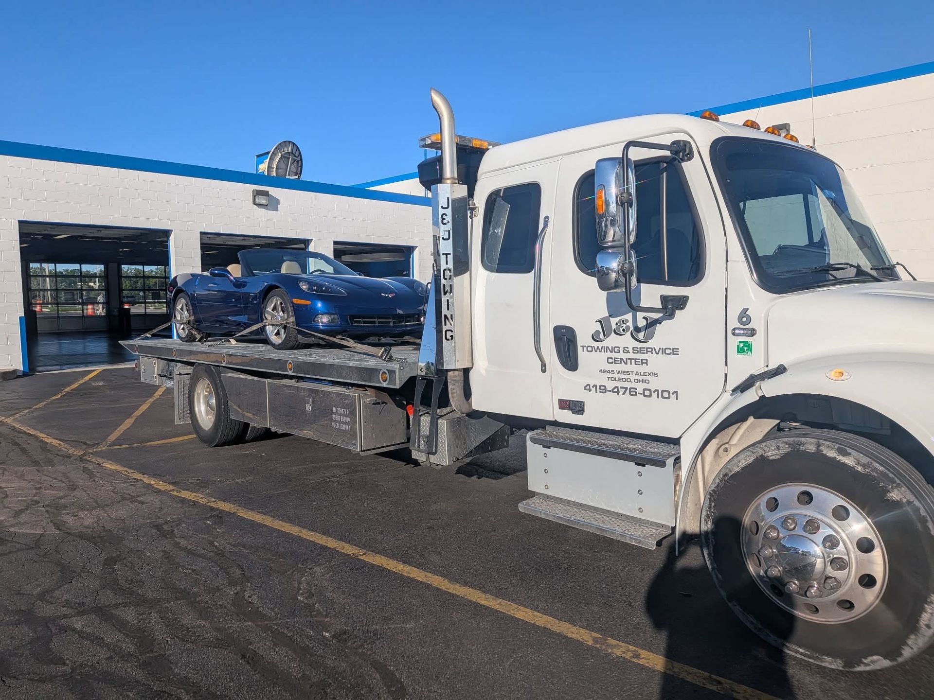 Tow truck carrying a blue sedan in a parking lot outside a building