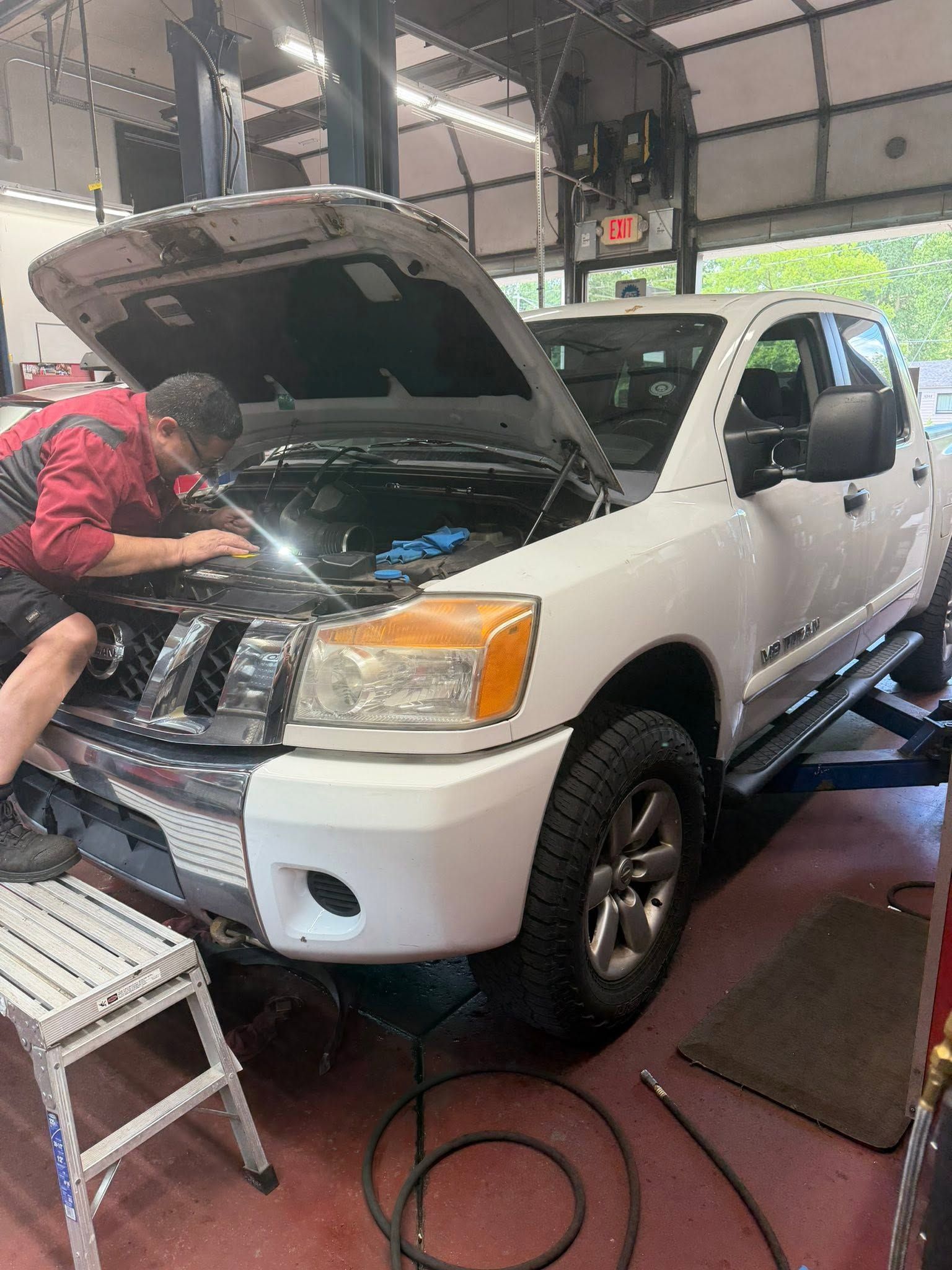 Mechanic working under the hood of a white pickup truck in a garage.