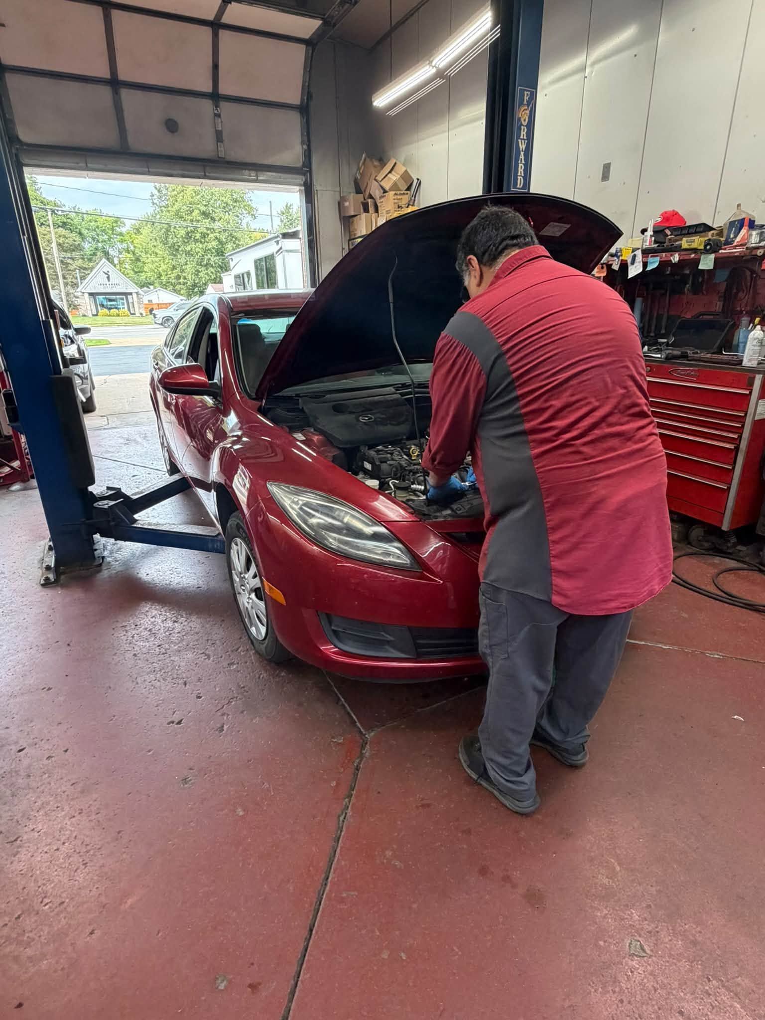 Mechanic inspecting a red car in an auto repair shop with the hood open