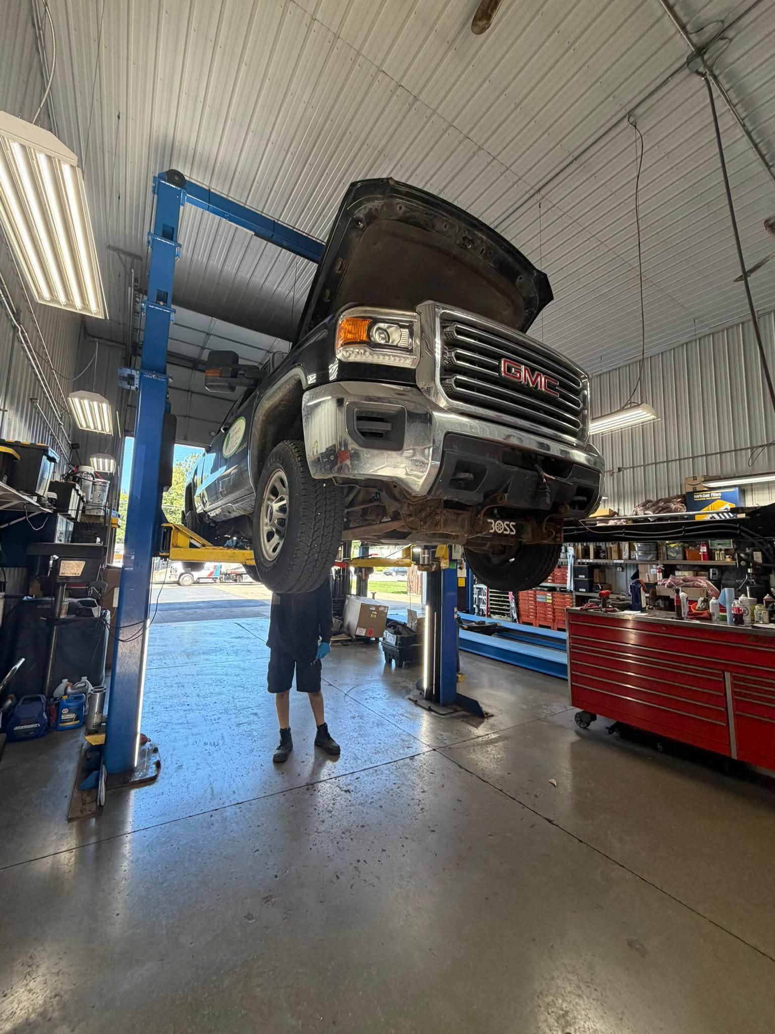 Pickup truck raised on a lift in an auto repair shop, with a mechanic underneath.