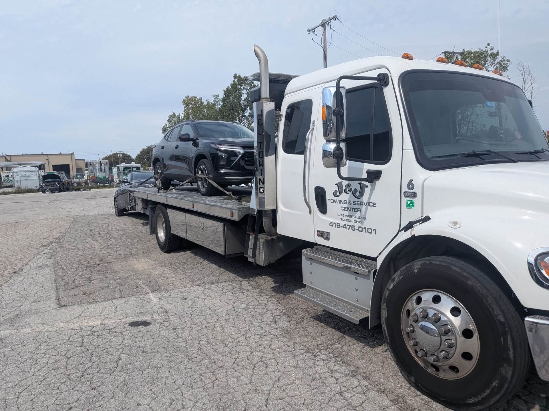 Tow truck carrying a black SUV on a flatbed in a gravel lot