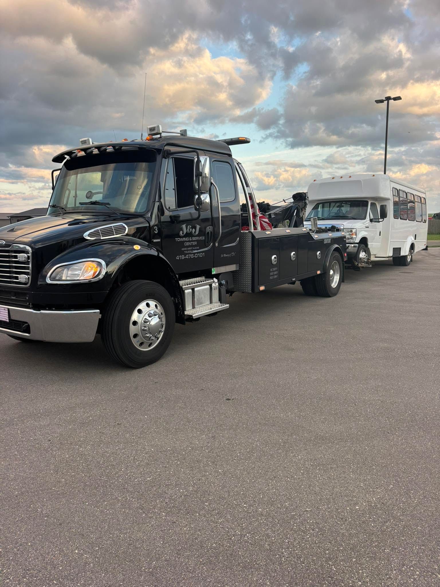 Black tow truck hauling a white travel trailer in a parking lot under a cloudy sky