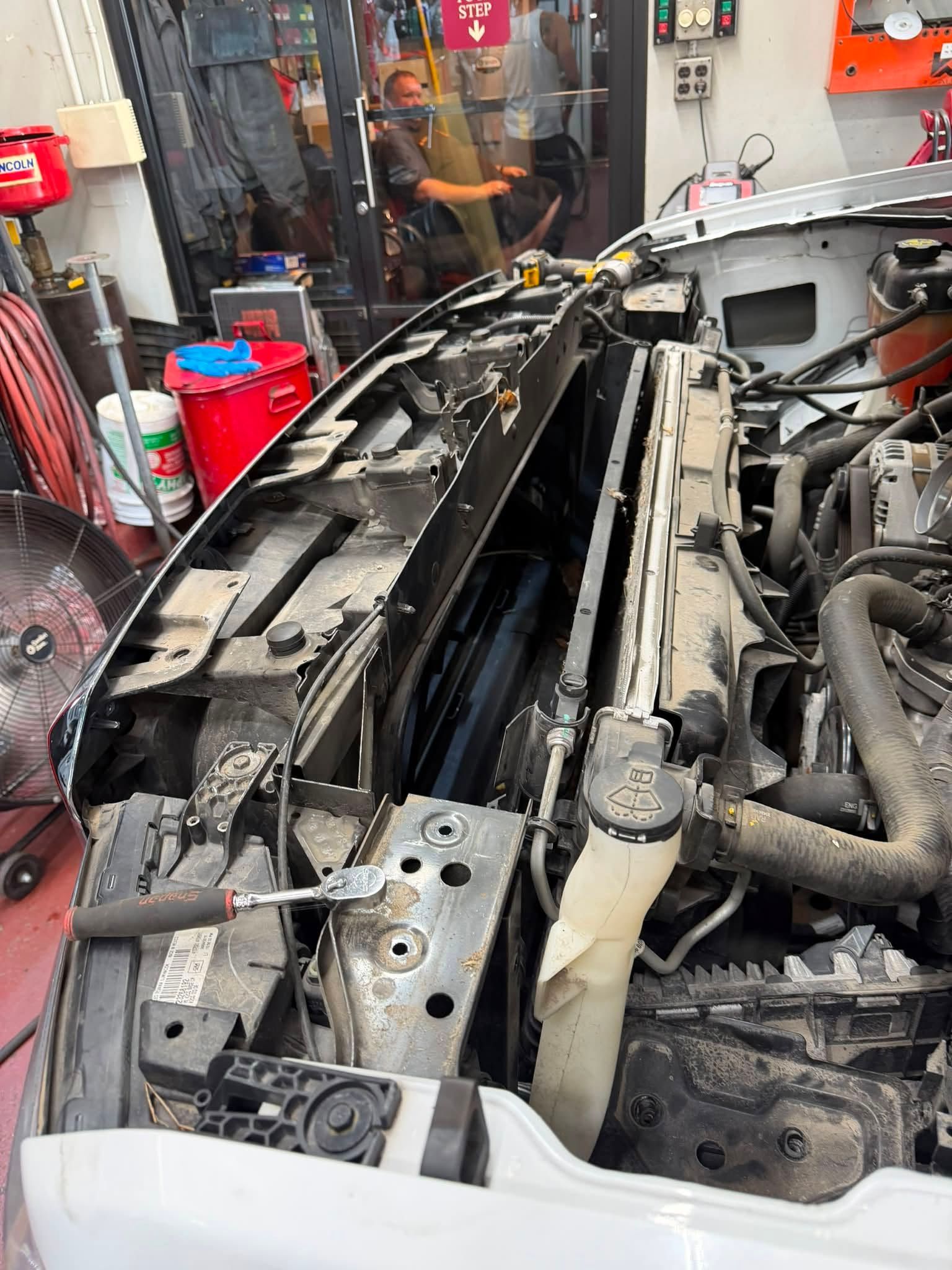 Car engine bay with front grille removed, showing exposed radiator support in a workshop under repair