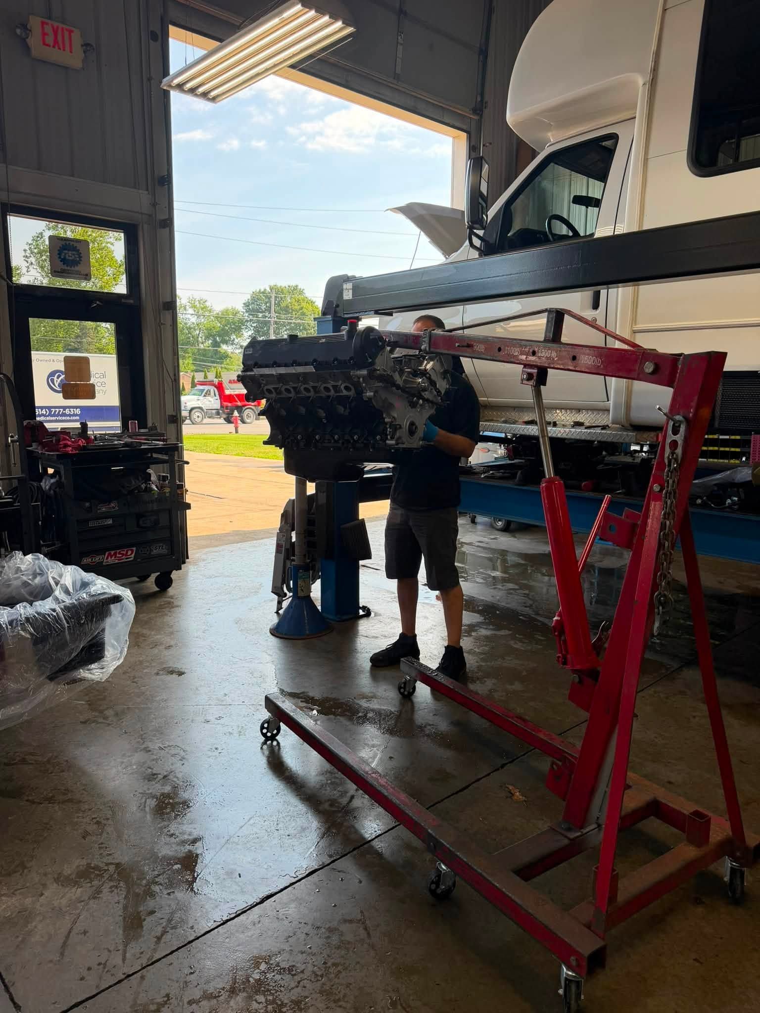Mechanic working under a vehicle on a red lift inside an auto repair shop