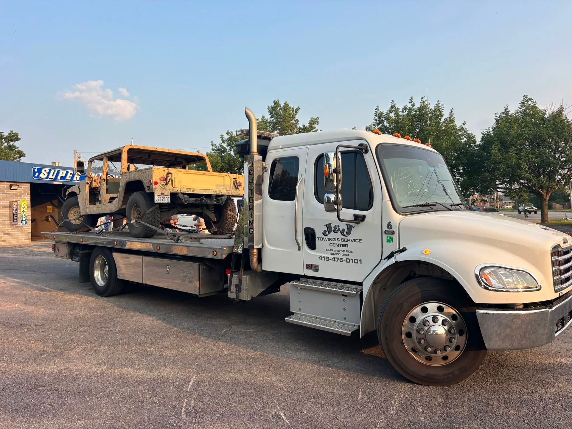 White tow truck hauling a yellow bulldozer in a parking lot at dusk