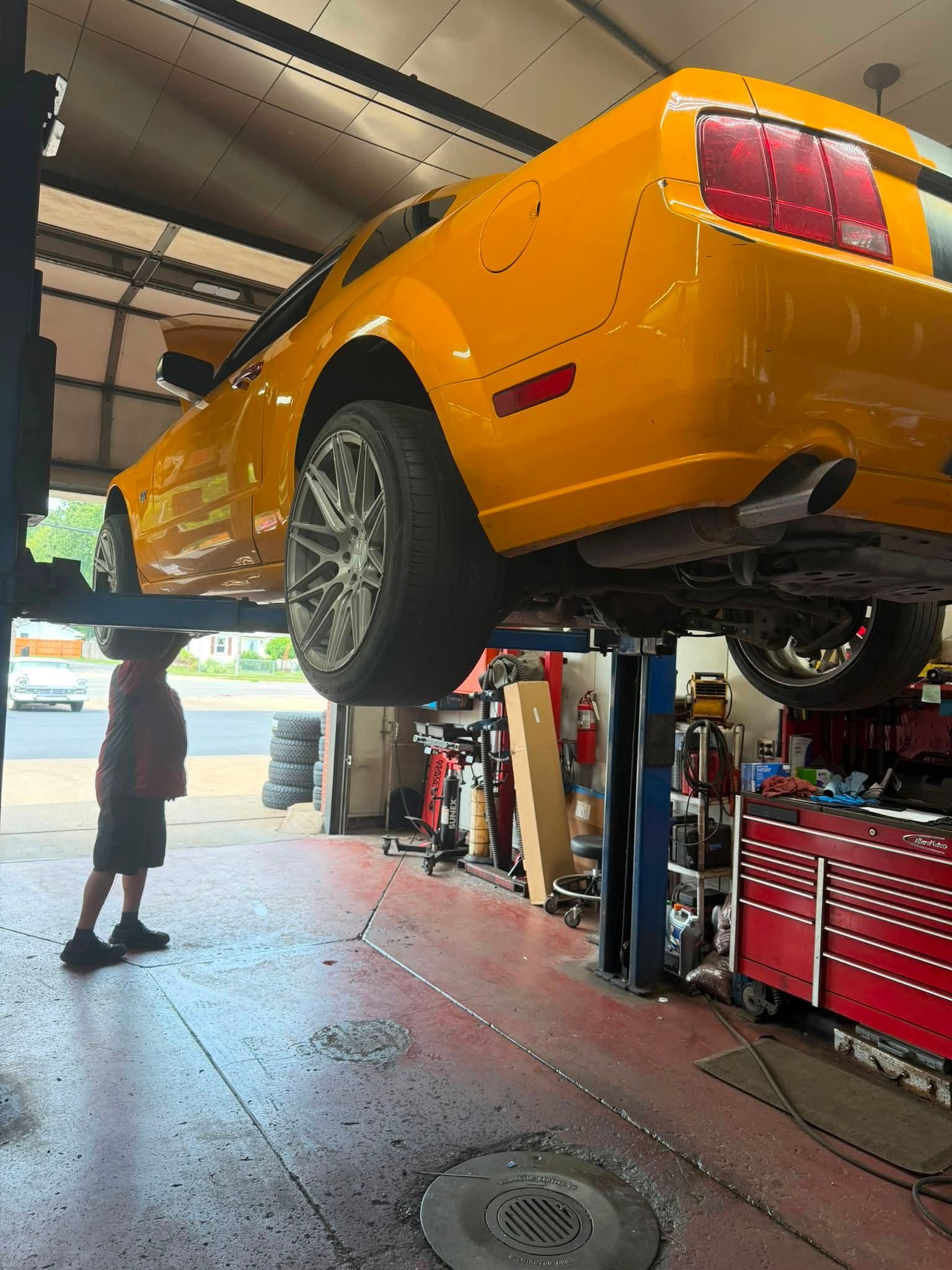 Yellow sports car lifted on a garage hoist, with a mechanic below