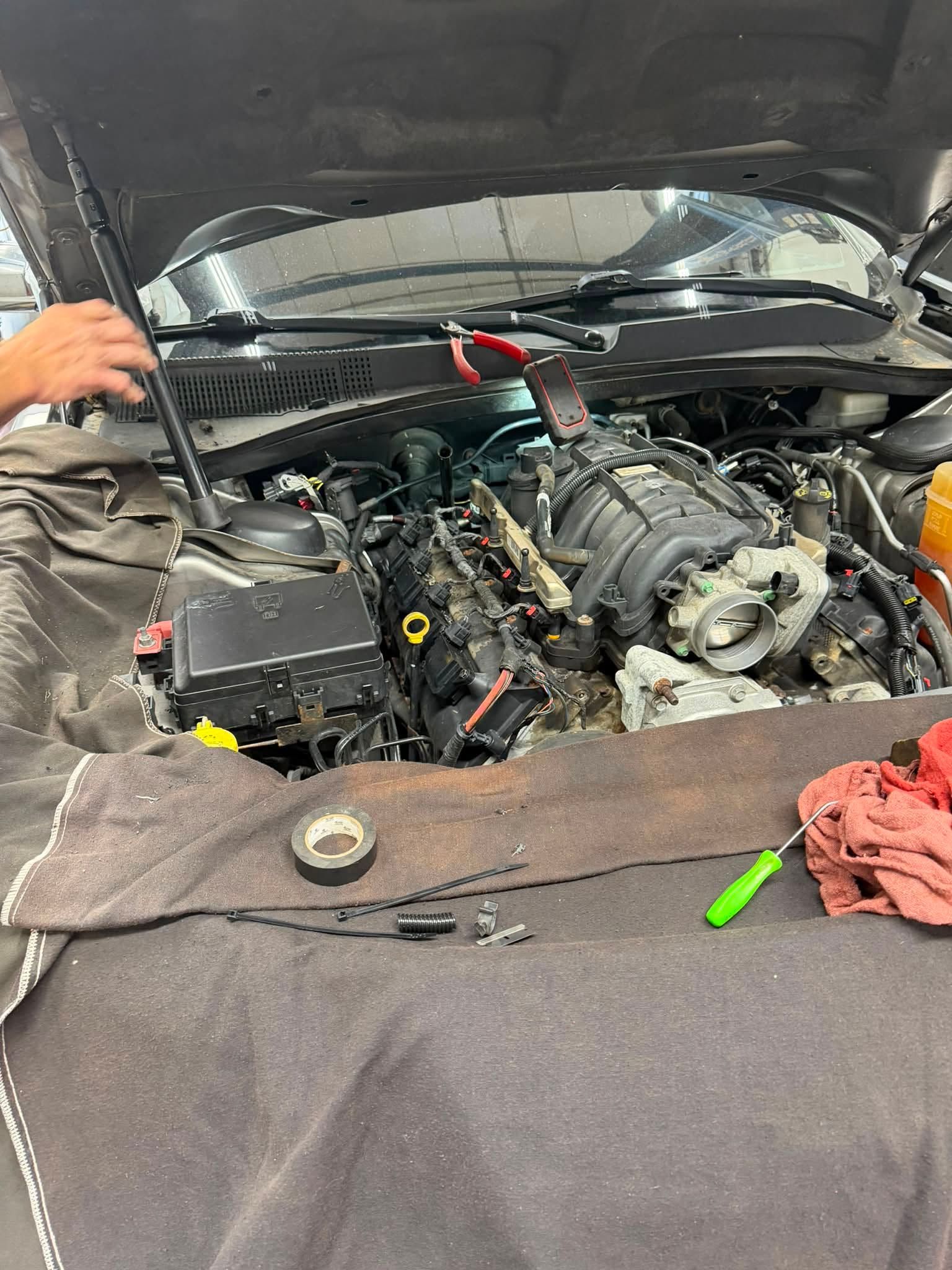 Car engine bay with exposed engine components and tools on a blanket, mid-repair indoors