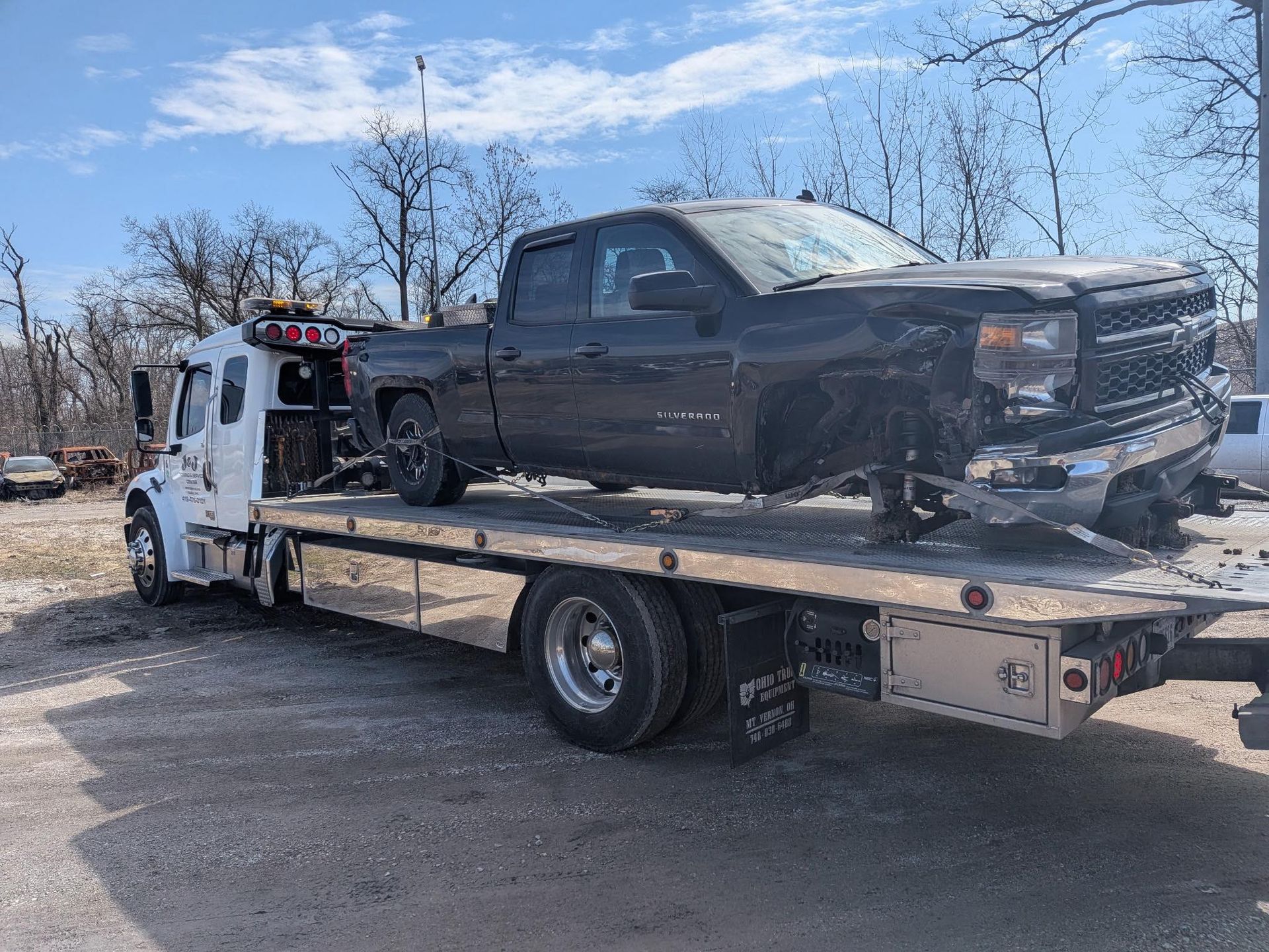 Tow truck carrying a black pickup on a flatbed in a parking lot