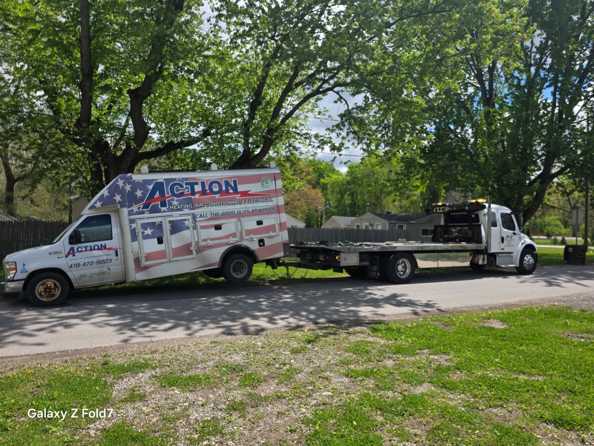 Tow truck carrying a white van on a roadside under leafy trees