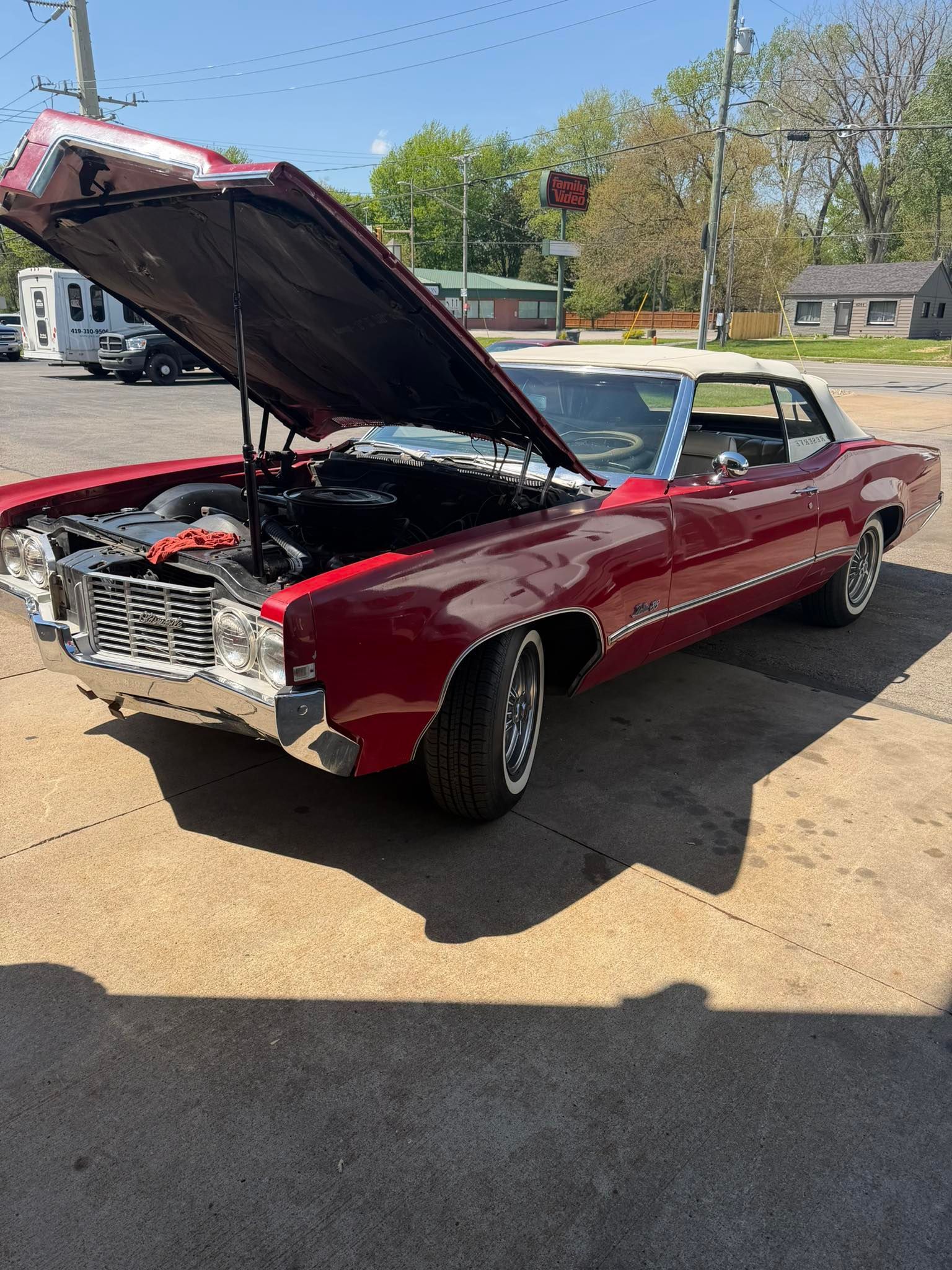 Red classic car with hood open at an outdoor car lot, showing the engine.