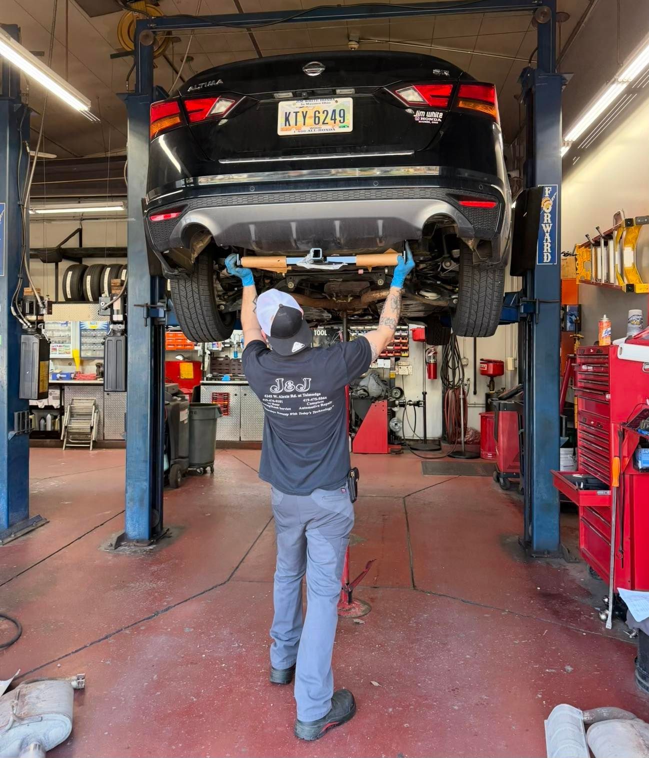 Mechanic inspecting a black sedan raised on a lift in an auto repair shop