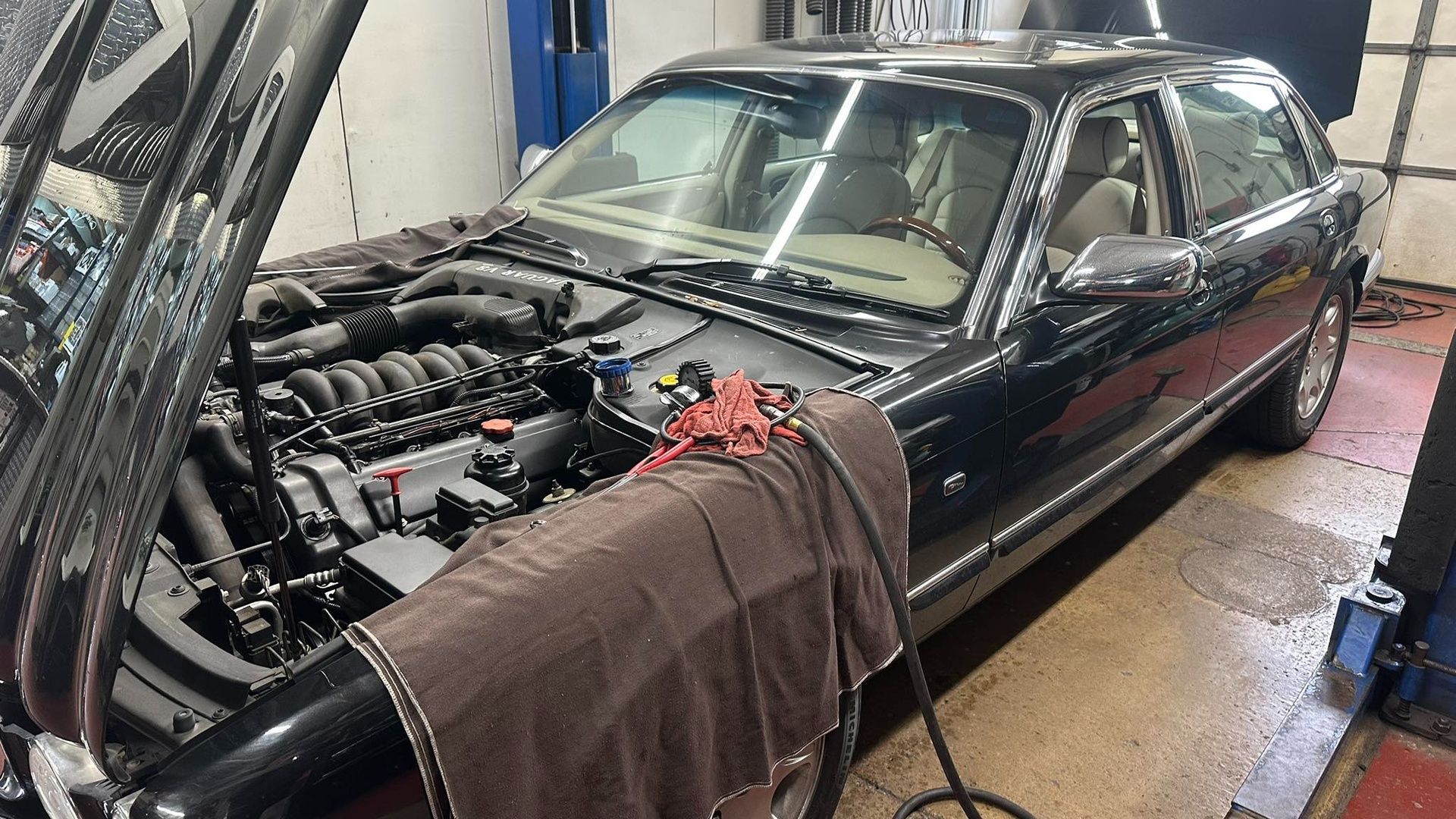 Black sedan in a garage with hood open, engine exposed, and a cloth draped over the front fender.