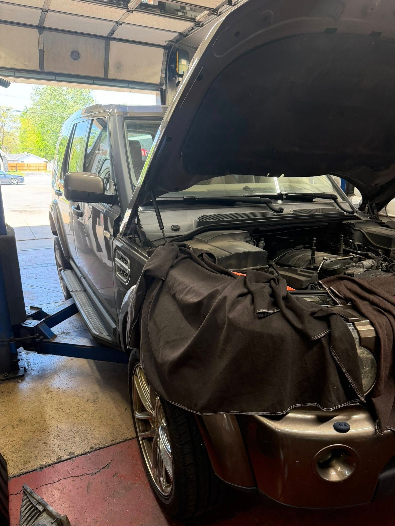 Black SUV in a garage with hood open and a large bag covering the front bumper