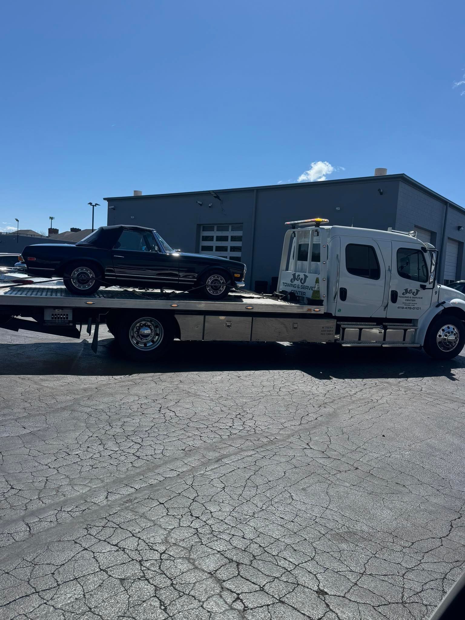 Tow truck hauling a black pickup truck in a gravel lot under a blue sky