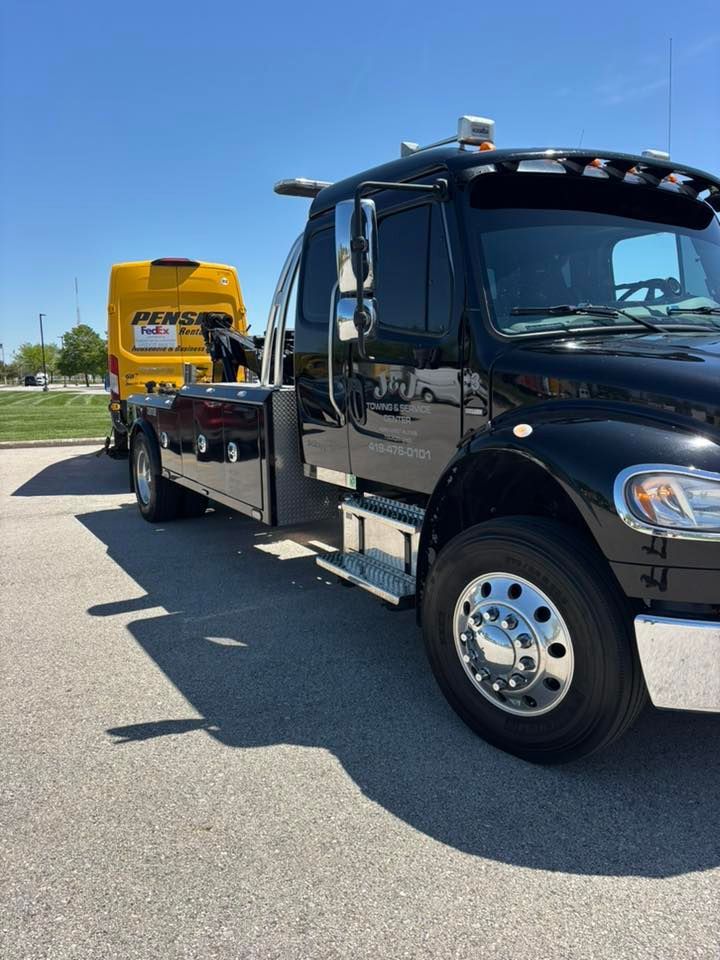 Black tow truck carrying a yellow truck on a sunny road