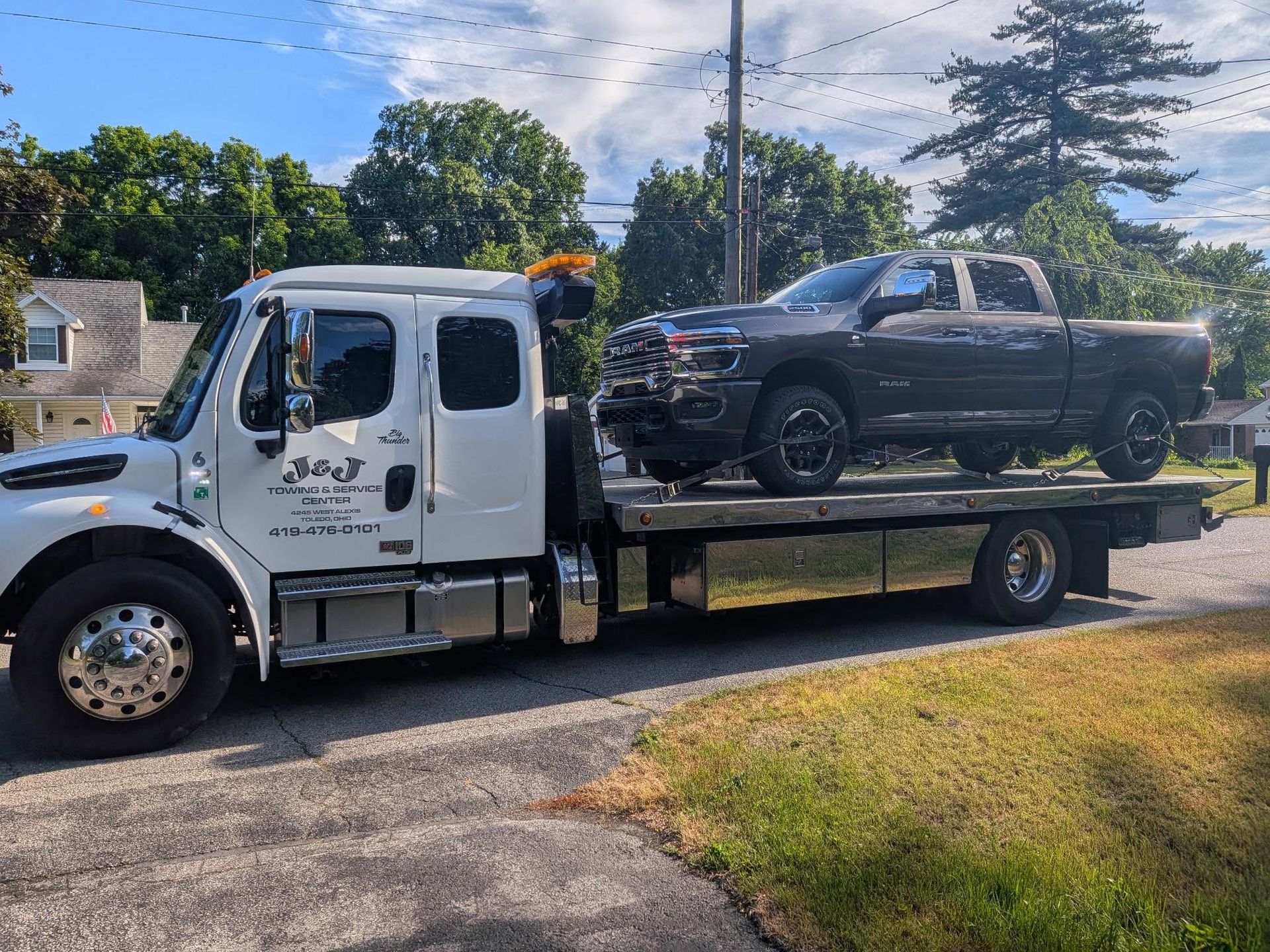 Tow truck carrying a black pickup on a flatbed along a roadside under a blue sky