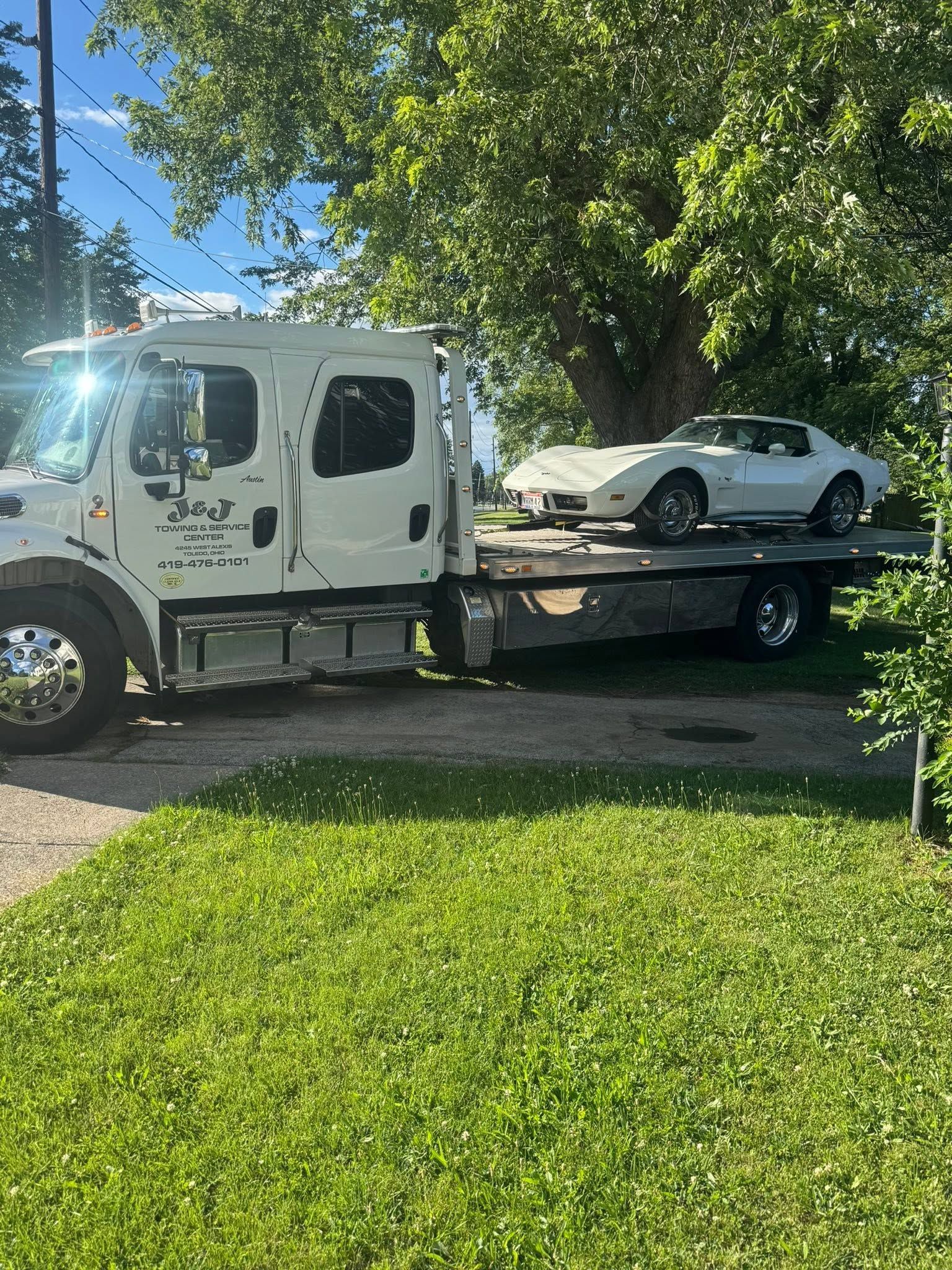 White tow truck carrying a white car on a flatbed in a sunny residential yard
