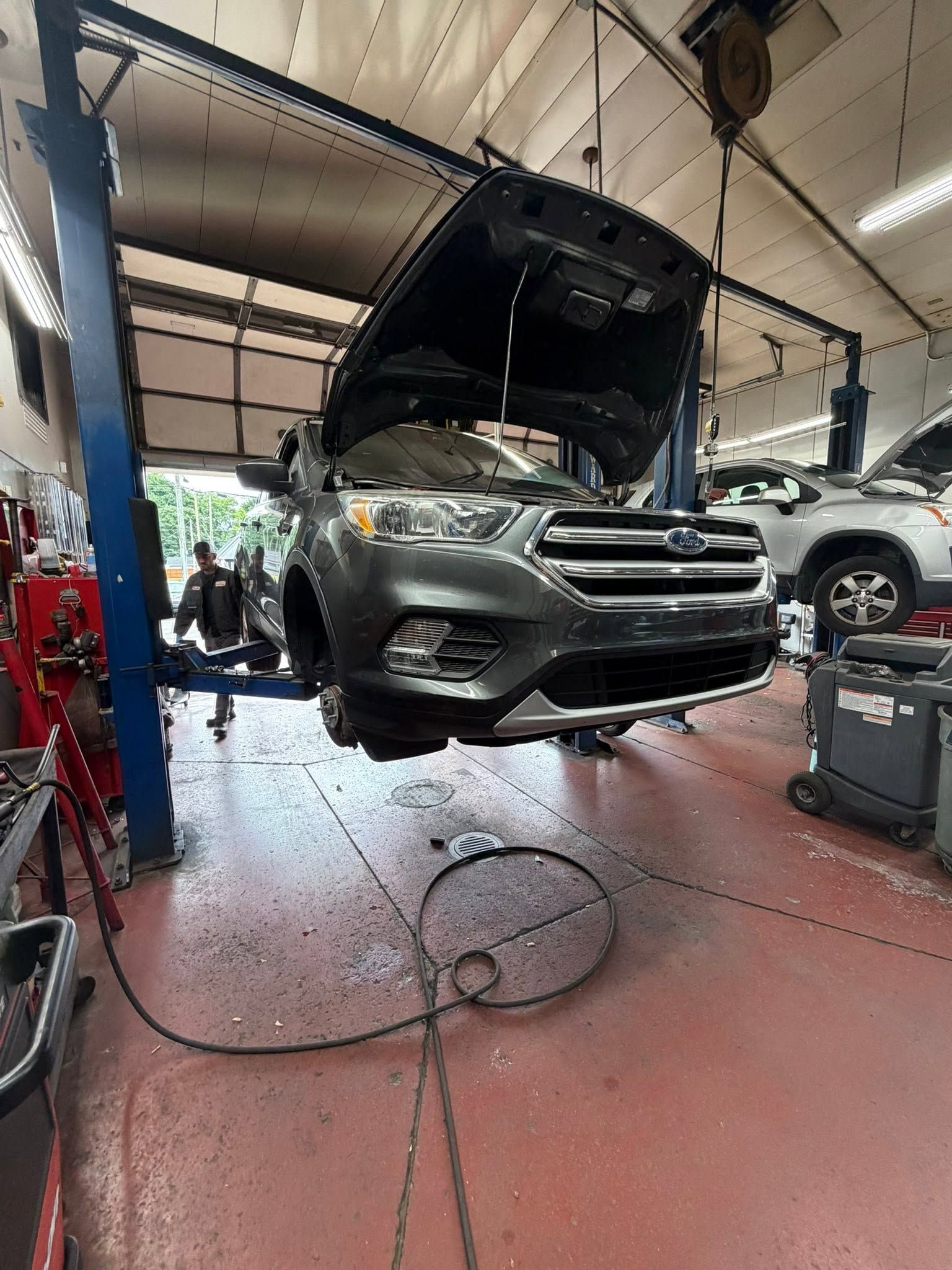 SUV in a garage with hood open, lifted for repair on a vehicle hoist.