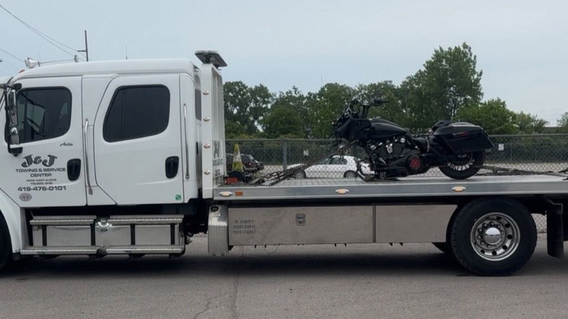 White flatbed tow truck hauling a black motorcycle on a highway.