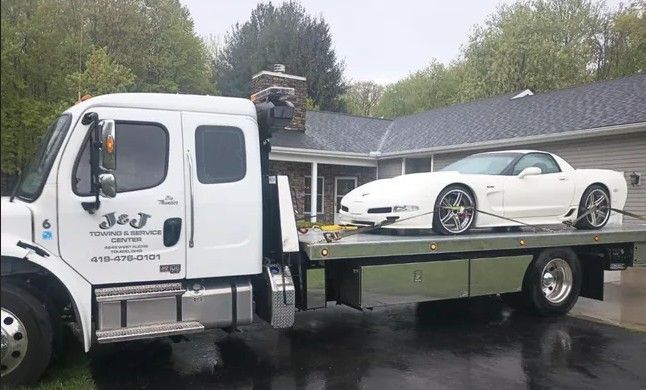 White Corvette loaded on a white tow truck in front of a house.