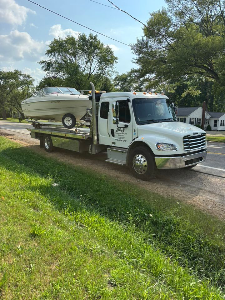 Tow truck carrying a white boat on a residential street, sunny day.