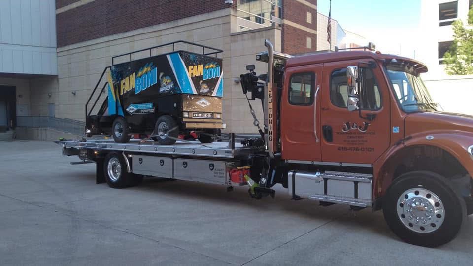 Tow truck with a black and blue vehicle on its flatbed, parked near a building.