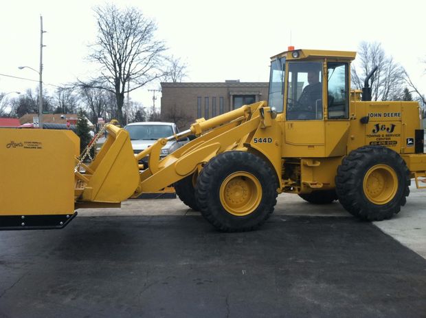 Yellow J-3 wheel loader plowing pavement; operator in cab.
