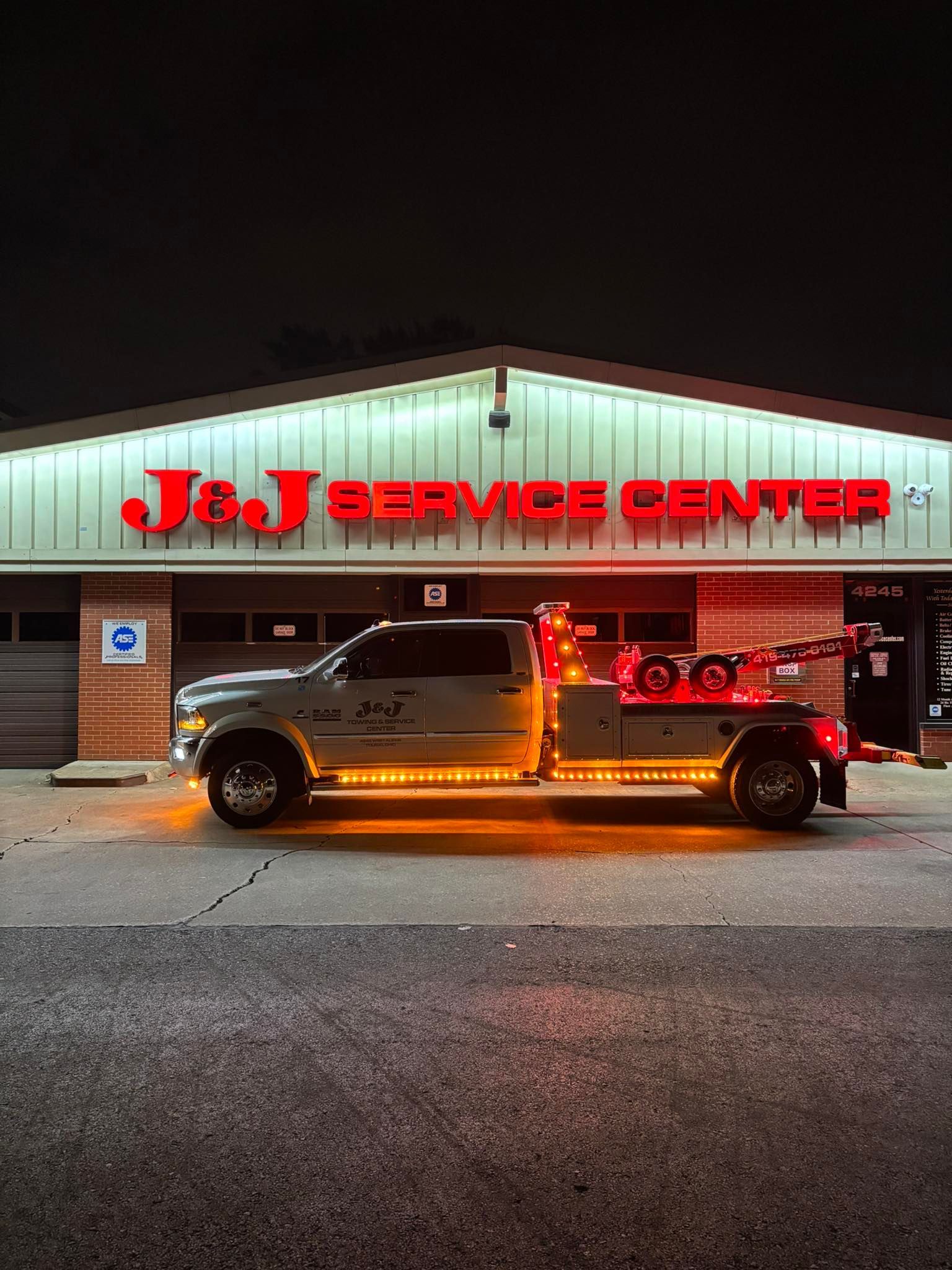 Tow truck with illuminated undercarriage parked in front of J&J Service Center at night. Red signage above the building.