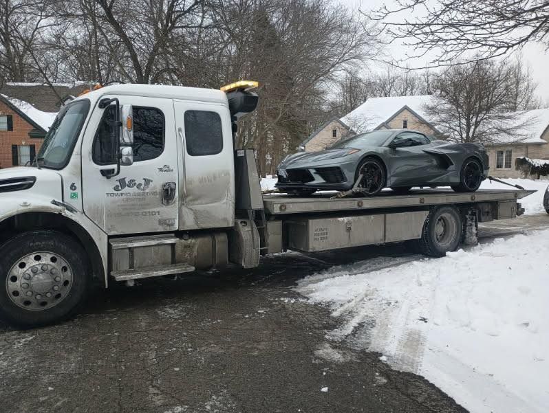Gray sports car on a flatbed tow truck in a snowy residential area.