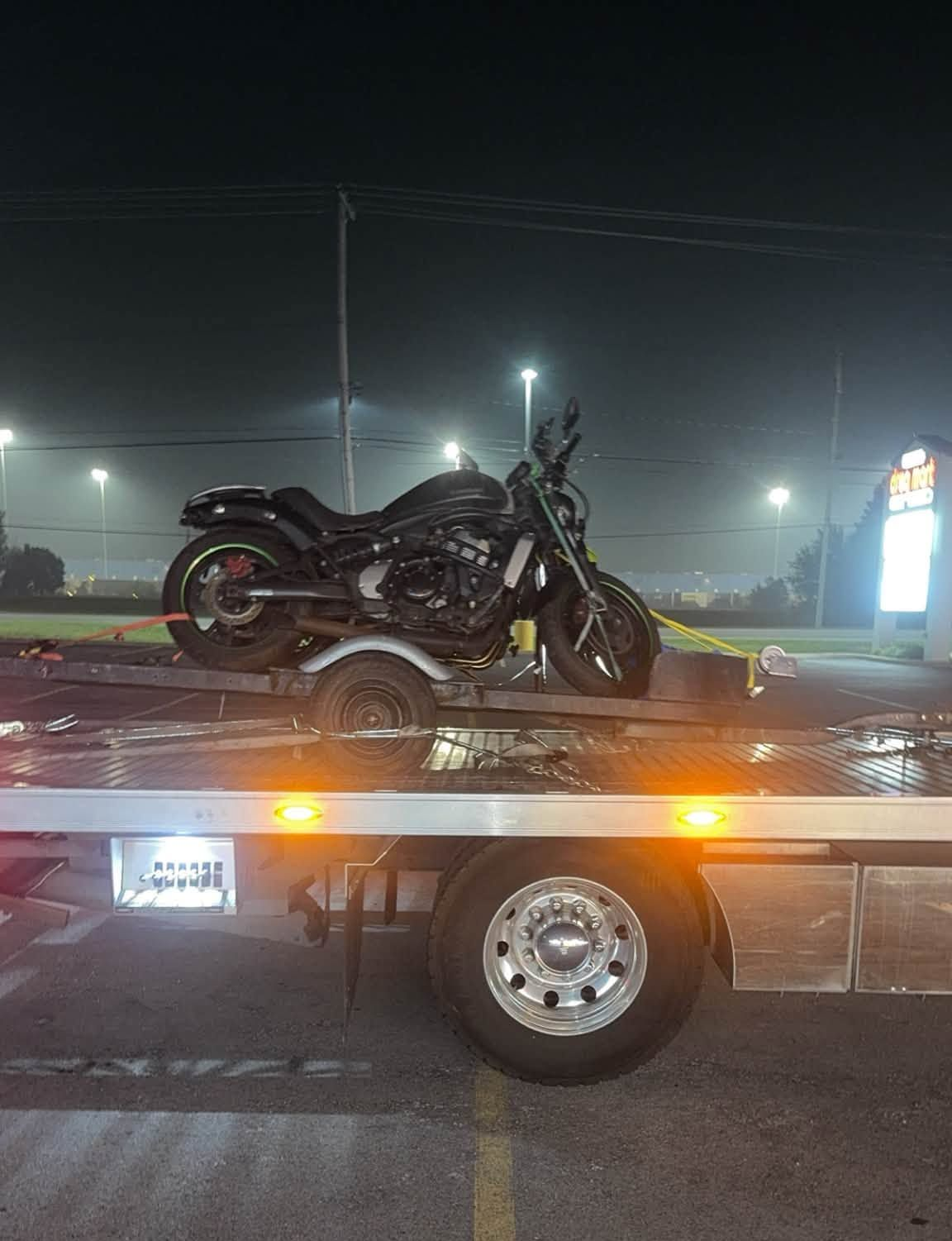 Damaged motorcycle on a tow truck at night, with flashing lights on a dark street.