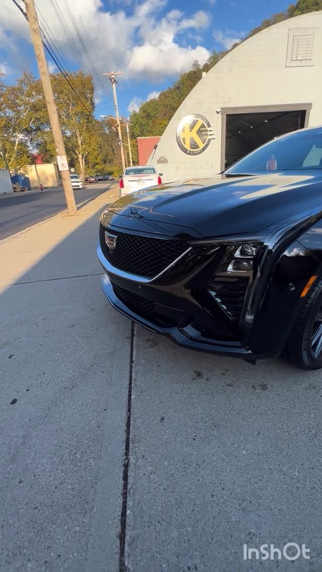 A black Cadillac parked in front of a building with a yellow logo, on a sunny day.