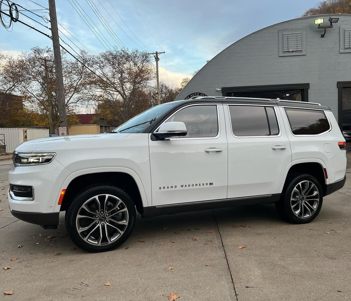 A white Jeep Grand Wagoneer was parked in front of a brick building on an overcast day.