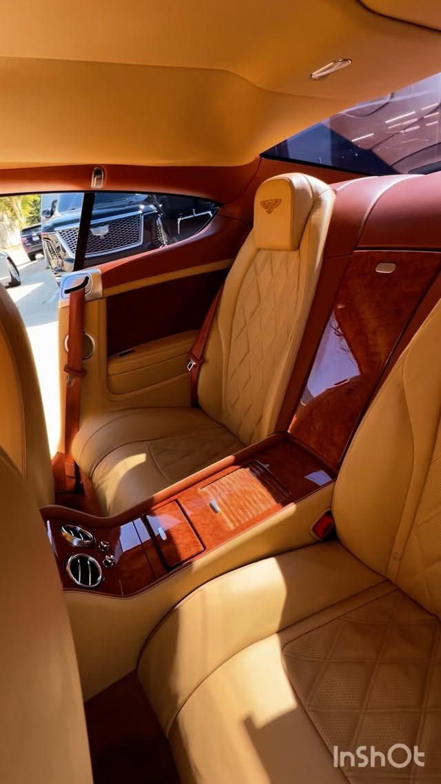 Tan leather interior of a luxury car, featuring wood paneling, rear seats, and a center console.